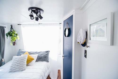 interior design four pillows on quilted white bed near blue door and window with white curtain inside well-lighted room bed